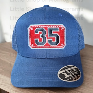May include: A blue trucker hat with a red and black embroidered patch that says "35". The hat has a mesh back and a Flexfit Tech label.