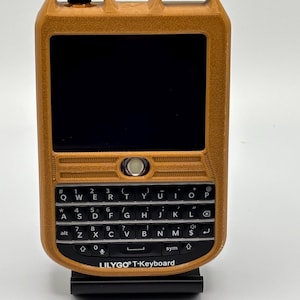 May include: A brown and black handheld device with a QWERTY keyboard and a small screen. The device is labeled "LILYGO T-Keyboard".
