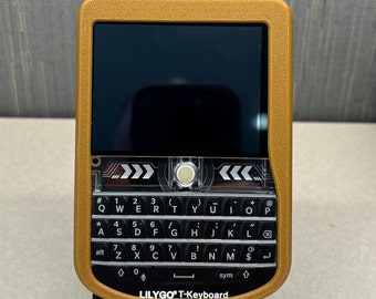 May include: A gold-colored handheld device with a black screen and a black keyboard. The keyboard has the letters QWERTYUIOP and numbers 123. The device has the text "LILYGO® T-Keyboard" on the bottom.