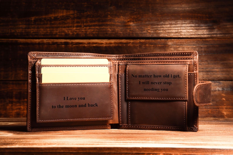 Puede incluir: Una cartera de cuero marr&oacute;n con dos mensajes grabados. El lado izquierdo dice "Te amo hasta la luna y de regreso". El lado derecho dice "No importa la edad que tenga, nunca dejar&eacute; de necesitarte".