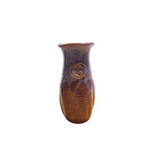 May include: A handcrafted ceramic vase with a brown and blue glaze. The vase has a unique shape with a flared top and a textured lower portion. A circular emblem is embossed on the front. This decorative vase is suitable for displaying flowers or as a standalone art piece.