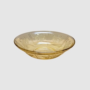 May include: A clear, amber-colored glass bowl with a floral design. The bowl has a shallow, rounded shape with etched floral patterns around the rim and on the sides. The glass is transparent, allowing light to pass through.