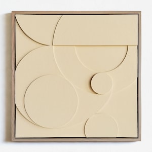 May include: A framed beige canvas with a geometric design of overlapping circles and semi-circles.