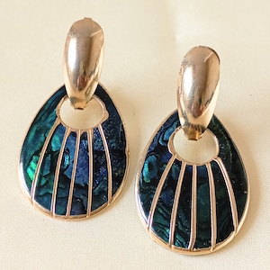 May include: A pair of gold-coloured earrings with a teardrop design. The earrings have a dark blue and teal iridescent inlay with vertical gold-coloured lines. The top section of the earrings is an oval shape.