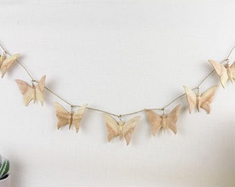 May include: A wooden butterfly garland with seven butterflies strung on twine. The butterflies are a light brown color and have a natural wood grain.