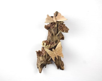 May include: A wooden wall decor featuring carved butterflies and flowers. The butterflies are light brown and the flowers are dark brown. The piece is mounted on a piece of driftwood.