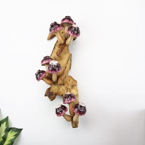 Pu&ograve; includere: Scultura decorativa in legno raffigurante funghi con cappelli bordeaux e pois bianchi. I funghi sono attaccati a un ramo di legno naturale marrone chiaro, creando un'opera d'arte stravagante ispirata alla natura.