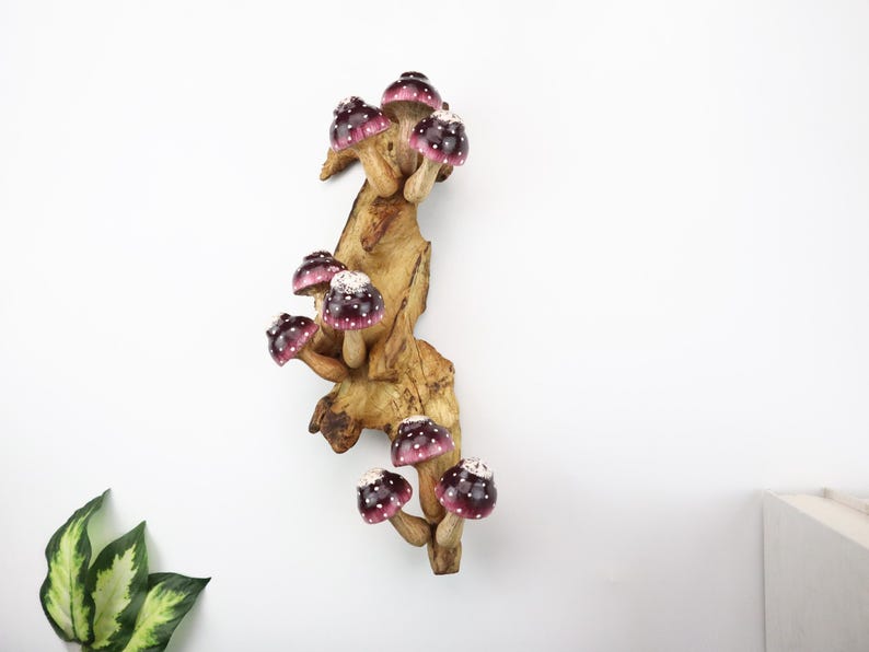 Pu&ograve; includere: Scultura decorativa in legno raffigurante funghi con cappelli bordeaux e pois bianchi. I funghi sono attaccati a un ramo di legno naturale marrone chiaro, creando un'opera d'arte stravagante ispirata alla natura.