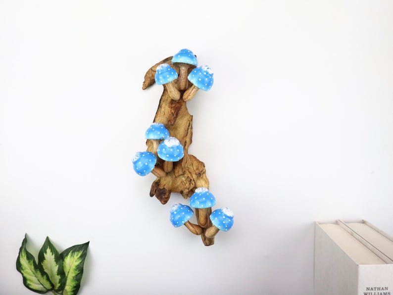 Pu&ograve; includere: Scultura in legno raffigurante funghi blu con pois bianchi. I funghi sono attaccati a un pezzo di legno naturale, creando un pezzo stravagante e decorativo. La scultura &egrave; posta su uno sfondo bianco.