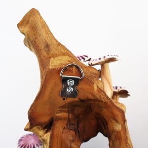 May include: A wooden wall hanging featuring a natural wood base with several mushroom sculptures. The mushrooms have white and purple caps. A metal hanger is attached to the back for easy display.