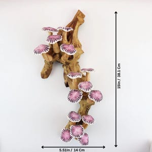 May include: A wooden wall hanging featuring a cluster of ceramic mushrooms with pink and white caps. The mushrooms are attached to a natural-looking, light brown wooden branch. The piece is 15 inches tall and 5.51 inches wide.