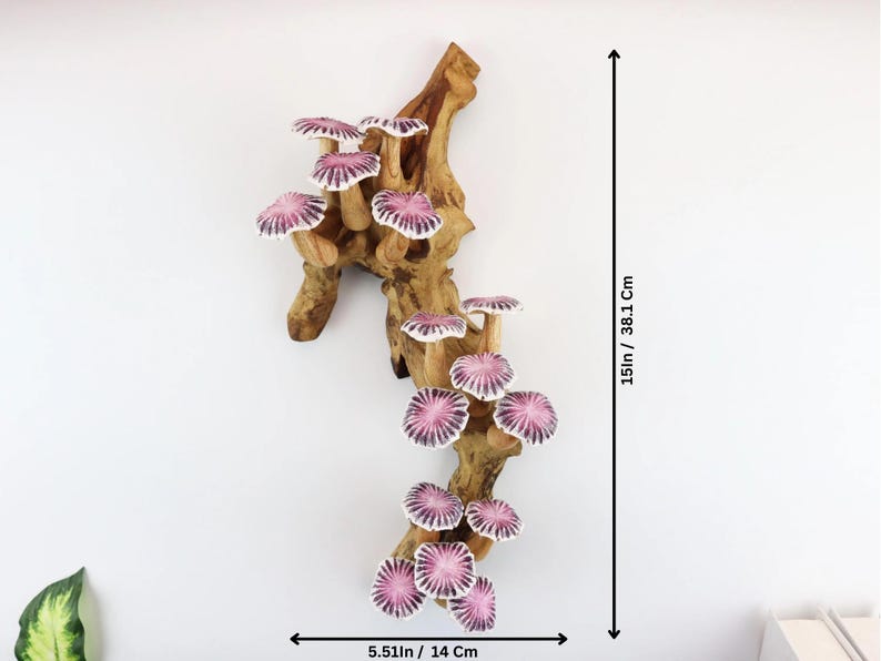 May include: A wooden wall hanging featuring a cluster of ceramic mushrooms with pink and white caps. The mushrooms are attached to a natural-looking, light brown wooden branch. The piece is 15 inches tall and 5.51 inches wide.