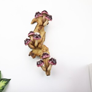 Pu&ograve; includere: Scultura decorativa in legno raffigurante un gruppo di funghi con cappelli bordeaux e pois bianchi. I funghi sono attaccati a una base di legno marrone chiaro dall'aspetto naturale, creando un design stravagante ispirato alla natura.