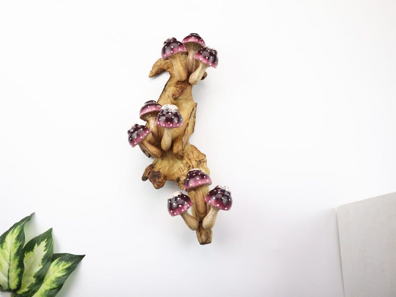 Pu&ograve; includere: Scultura decorativa in legno raffigurante un gruppo di funghi con cappelli bordeaux e pois bianchi. I funghi sono attaccati a una base di legno marrone chiaro dall'aspetto naturale, creando un design stravagante ispirato alla natura.