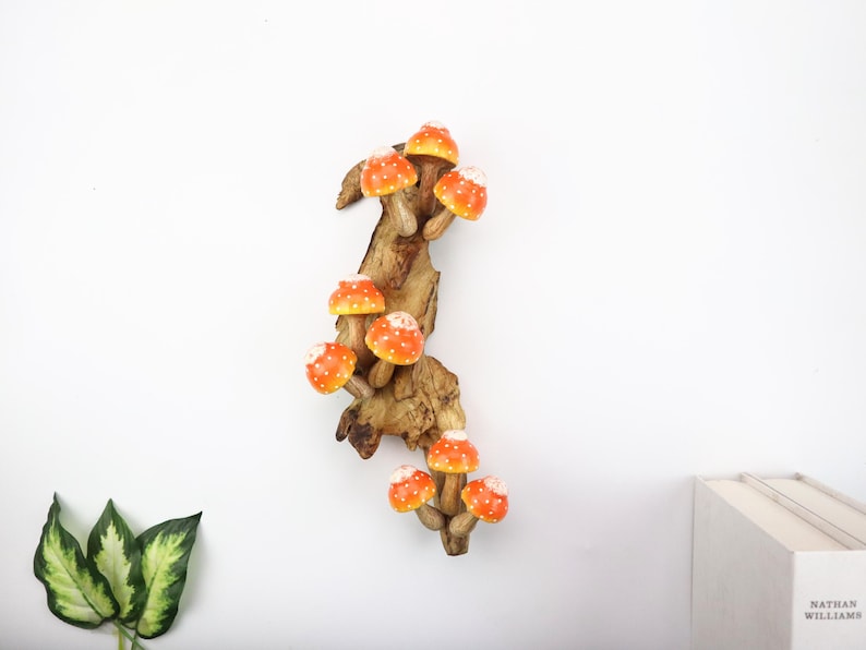 Pu&ograve; includere: Una scultura decorativa in legno con diversi funghi arancioni e bianchi a pois attaccati a un pezzo di legno. I funghi hanno un aspetto luminoso e il legno ha un aspetto naturale e strutturato.