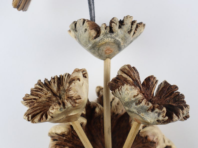 K&ouml;nnte beinhalten: Nahaufnahme einer Holzblumenskulptur. Die Skulptur zeigt drei bl&uuml;tenartige Formen mit aufwendigen, strukturierten Details in Braun- und Beiget&ouml;nen. Jede Bl&uuml;te ist auf einem schlanken Holzstiel befestigt, mit einer vierten Bl&uuml;te im Hintergrund. Der Hintergrund ist wei&szlig;.