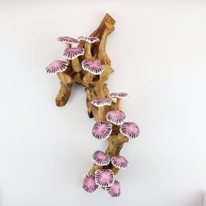 May include: A decorative wooden wall hanging featuring a natural wood branch adorned with several ceramic mushrooms. The mushrooms have pink caps with white edges and dark purple accents. The wood has a light brown color.