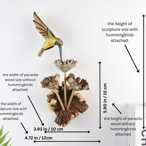 K&ouml;nnte beinhalten: Holzskulptur eines Kolibris mit gelb-braunem K&ouml;rper &uuml;ber stilisierten Blumen. Die Skulptur ist auf Parasitenholz montiert. Die Skulptur ist 26 cm hoch und 12 cm breit.