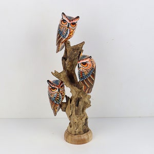 Puede incluir: Una escultura de madera de tres b&uacute;hos posados en una rama de &aacute;rbol. Los b&uacute;hos est&aacute;n pintados en tonos de naranja, marr&oacute;n, azul y negro. La escultura es una pieza decorativa para el hogar o la oficina.