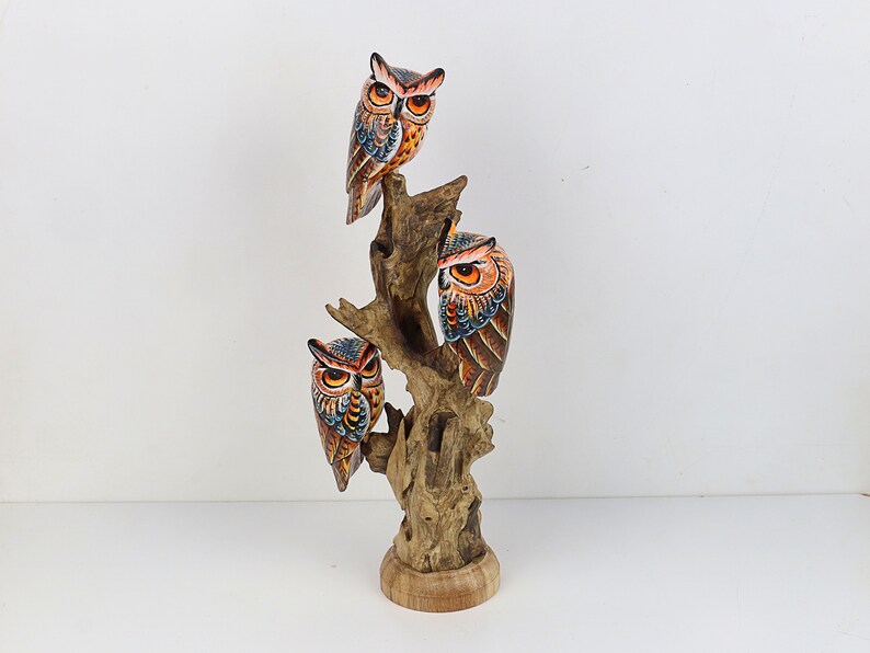 Puede incluir: Una escultura de madera de tres b&uacute;hos posados en una rama de &aacute;rbol. Los b&uacute;hos est&aacute;n pintados en tonos de naranja, marr&oacute;n, azul y negro. La escultura es una pieza decorativa para el hogar o la oficina.