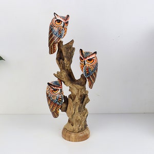 Puede incluir: Una escultura de madera de b&uacute;ho con tres b&uacute;hos posados en una rama de &aacute;rbol. Los b&uacute;hos est&aacute;n pintados en tonos de marr&oacute;n, naranja y azul con detalles intrincados. La escultura es una pieza decorativa para un hogar u oficina.
