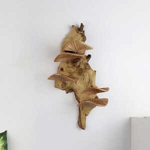K&ouml;nnte beinhalten: Eine Wandskulptur aus Holz mit einer nat&uuml;rlichen braunen Oberfl&auml;che. Die Skulptur verf&uuml;gt &uuml;ber mehrere Schichten aus geschnitzten Pilzformen, die ein einzigartiges und organisches Design schaffen.