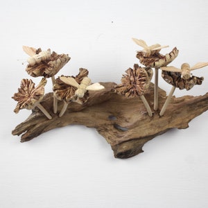 Op de afbeelding: Een houten wandkunstwerk met gesneden vlinders en bloemen op een drijfhoutbasis. De vlinders zijn in de vlucht en de bloemen bloeien. Het stuk is geschilderd in tinten bruin en beige.