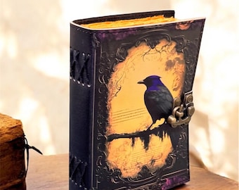 Può includere: Un diario rilegato in pelle blu scuro con un'illustrazione di uccello in stile vintage sulla copertina. Il diario ha una chiusura in metallo e cuciture decorative.