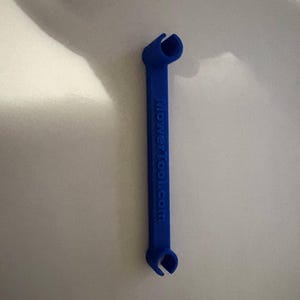 May include: A blue tool with curved ends and the text "mowertool.com" printed on the side. The tool has a long, rectangular body and is likely used for a specific mechanical purpose.