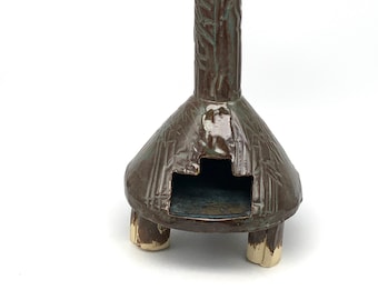May include: A small, brown ceramic fireplace with a chimney and four legs. The fireplace has a textured surface and a small opening in the front.