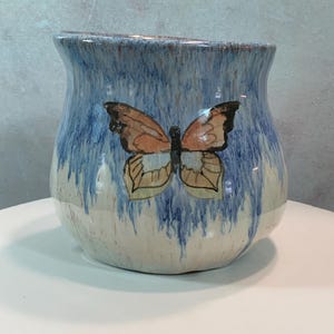 May include: A blue and white ceramic planter with a painted butterfly design. The butterfly has orange wings and a black body.