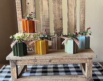 May include: A rustic wooden bench with a black and white checkered rug underneath.  The bench is decorated with small wooden pumpkins in various colors, including green, yellow, orange, gray, and blue.  Each pumpkin has a small sprig of greenery and red berries on top.