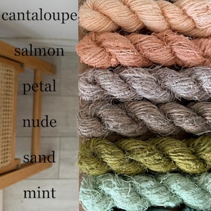 May include: A vertical display of eight skeins of yarn in various colors. The colors include ivory, cantaloupe, salmon, petal, nude, sand, mint, and sky blue. The yarn is tightly wound and appears to be made of a natural fiber.