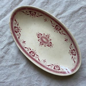 Peut inclure: Plat ovale de service avec une base crème et un motif floral bordeaux. La bordure et le motif central présentent des motifs complexes. L'assiette est en céramique ou en porcelaine et convient pour servir des aliments.