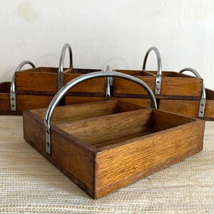 Peut inclure: Plateau de service en bois avec un intérieur divisé et une poignée en métal incurvée. Le plateau est en bois teinté et de forme rectangulaire. Plusieurs plateaux sont visibles, suggérant un ensemble.