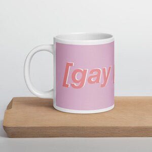 May include: A pink ceramic mug with the text "[gay]" in a pink and white font.