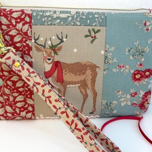 May include: A rectangular pouch with a gold zipper and a matching wrist strap. The pouch features a patchwork design with a deer illustration, floral patterns, and a red and beige botanical print. The wrist strap is 10 inches long.