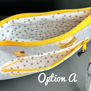 Puede incluir: Una bolsa gris con cremallera amarilla y forro estampado blanco y gris. La bolsa tiene dos compartimentos y presenta un peque&ntilde;o estampado de animales. El texto "Opci&oacute;n A" es visible en la imagen.