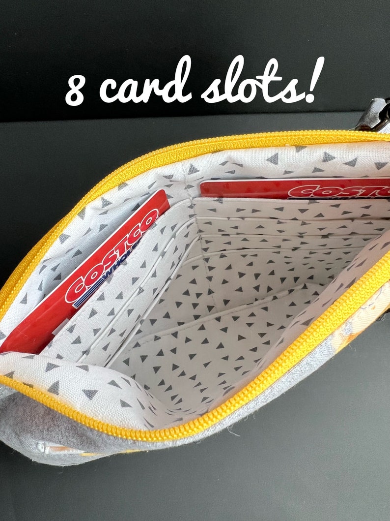 Puede incluir: Una bolsa con cremallera amarilla y gris con 8 ranuras para tarjetas. La bolsa est&aacute; abierta y el interior est&aacute; forrado con una tela gris con peque&ntilde;os tri&aacute;ngulos blancos. Dos tarjetas rojas con la palabra "Costco" son visibles en las ranuras.