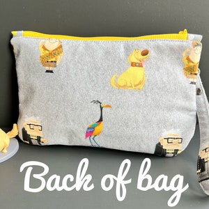 Puede incluir: Bolsa de cremallera gris con una cremallera amarilla y una correa amarilla. La bolsa tiene una variedad de personajes de dibujos animados coloridos impresos en ella, incluyendo un perro, un p&aacute;jaro y un hombre con gafas. El texto "Back of bag" est&aacute; escrito en blanco sobre un fondo gris debajo de la bolsa.
