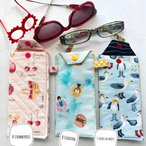 May include: Three pairs of eyeglasses and three fabric eyeglass cases. The cases are labeled "A Strawberries", "B Floating", and "C Birds in Boots". The cases have different patterns and colors, including pink, blue, and white.
