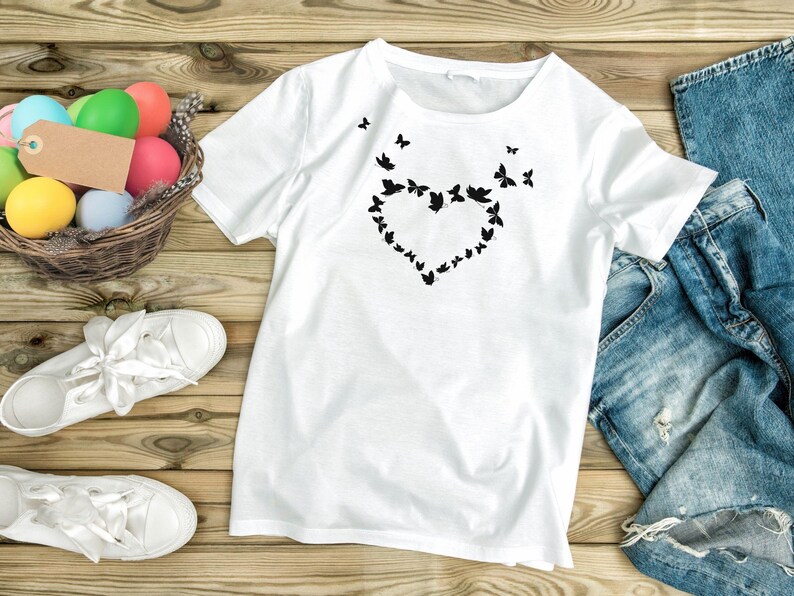 Puede incluir: Camiseta blanca con un dise&ntilde;o de mariposa negra en forma de coraz&oacute;n.