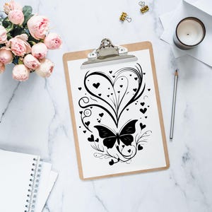Puede incluir: Una ilustraci&oacute;n en blanco y negro de una mariposa con un dise&ntilde;o en forma de coraz&oacute;n y acentos florales. La ilustraci&oacute;n est&aacute; sobre un fondo blanco y est&aacute; enmarcada por un portapapeles.