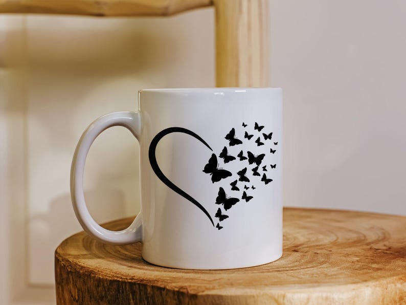 Puede incluir: Taza de cer&aacute;mica blanca con una silueta negra de un coraz&oacute;n lleno de mariposas. La taza tiene un asa negra.