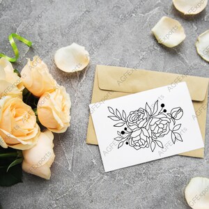 以下が含まれることがあります： 白いカードに、黒と白の線画で描かれた花束。カードは茶色の封筒の上に置かれている。封筒は灰色のざらざらした表面の上に置かれている。カードの周りに白いバラの花びらが散らばっている。