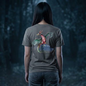 Könnte beinhalten: Ein graues T-Shirt mit einem farbenfrohen Drachendesign auf dem Rücken. Der Drache hat rote, grüne und rosa Akzente, mit einem langen Schwanz und ausgebreiteten Flügeln. Das Shirt wird mit einer blauen Jeans kombiniert.
