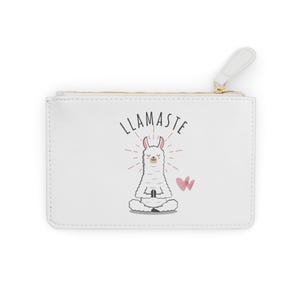 Op de afbeelding: Witte etui met ritssluiting met een gouden rits en een witte treklip. De etui heeft een cartoon lama die mediteert met het woord "LLAMASTE" erboven en een roze vlinder. De etui is rechthoekig.