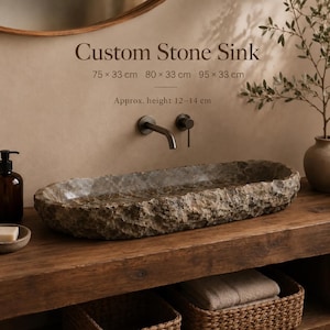 Könnte beinhalten: Ein ovales Steinwaschbecken mit rauer, strukturierter Außenseite und glattem Innenbecken. Text: Custom Stone Sink, 75 x 33 cm, 80 x 33 cm, 95 x 33 cm, Approx. height 12-14 cm. Das Waschbecken steht auf einer Holzoberfläche mit dunkler Armatur.