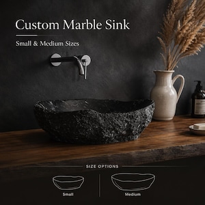 May include: A custom marble sink with a textured, dark gray finish. The image shows a small and medium size option. The sink is set on a wooden surface, with a chrome faucet mounted on the dark wall behind it.