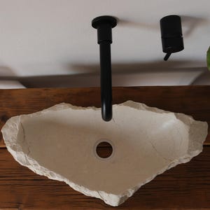 Hand-carved Crema Marfil marble sink with glossy inner bowl and raw edge, installed on rustic wood vanity.